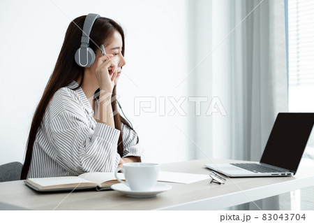 Video call, a young Asian woman wearing headphones, communicates via online video long distance, looking at the digital laptop screen, happily greeted with a friend 83043704