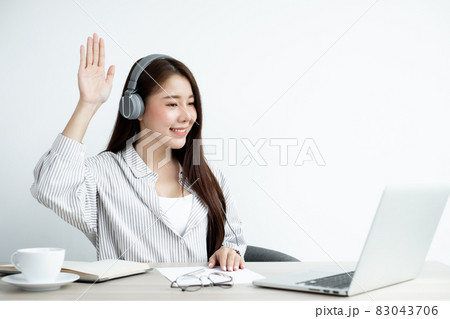 Video call, a young Asian woman wearing headphones, communicates via online video long distance, looking at the digital laptop screen, happily greeted with a friend 83043706