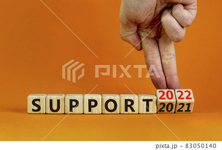 Symbol of planning 2022 support new year. Businessman turns a wooden cube and changes words 'support 2021' to 'support 2022'. Beautiful orange background, copy space. Business, 2022 support concept. Symbol of planning 2022 support new year. Businessman turns a wooden cube and changes words 'support 2021' to 'support 2022'. Beautiful orange background, copy space. Business, 2022 support concept. 83050140