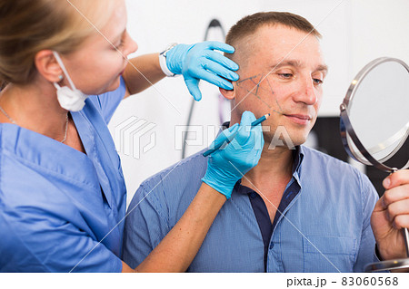 Female specialist is marking zone on face of client 83060568