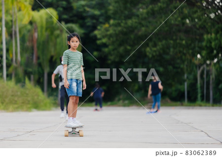 Asian child girl learning to skateboard outdoors. Kid having fun and playing skateboard on the road at the day time. Kid activity and extreme sport concept. 83062389