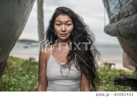 Portrait of beautiful young mongol woman in white dress standing between two old wooden ships. Looking at camera with copy space. Romantic portrait. Portrait of beautiful young mongol woman in white dress standing between two old wooden ships. Looking at camera with copy space. Romantic portrait. 83062432