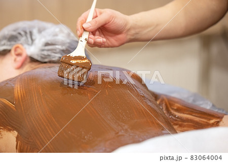 Massagist applies melted chocolate to woman's back 83064004