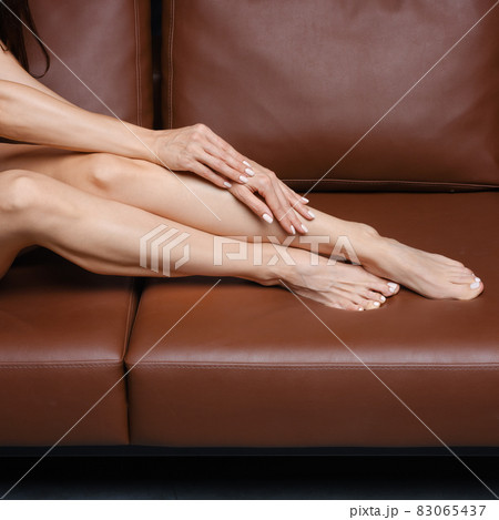 Middle age woman sits on sofa in black bodysuit and warm overknee socks 83065437