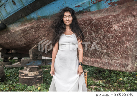 Portrait of mongol beautiful woman with natural long curtly hair. Looking at camera with copy space. Light grey silky dress. Blurred background. Portrait of mongol beautiful woman with natural long curtly hair. Looking at camera with copy space. Light grey silky dress. Blurred background. 83065846