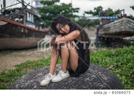 Sitting on the stone, holding her legs and relaxing. Brunette with long hair posing. Looking at camera with copy space. . High quality photo 83066075