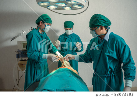 Surgeons team performing surgery and passing surgical scissors on injured patient in operating room Surgeons team performing surgery and passing surgical scissors on injured patient in operating room 83073293
