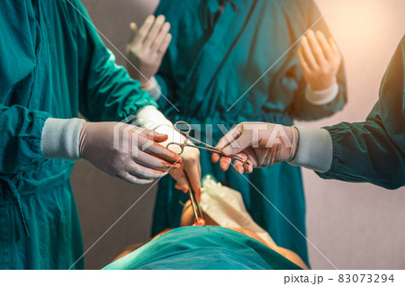 Surgeons team performing surgery and passing surgical scissors on injured patient in operating room Surgeons team performing surgery and passing surgical scissors on injured patient in operating room 83073294