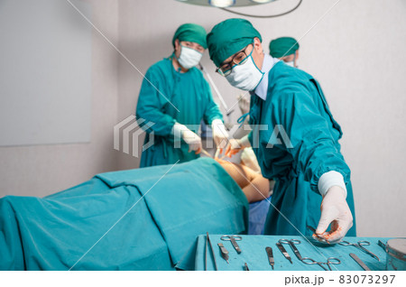 Team surgeon choosing scalpel while operating seriously injured patient in operating room Team surgeon choosing scalpel while operating seriously injured patient in operating room 83073297