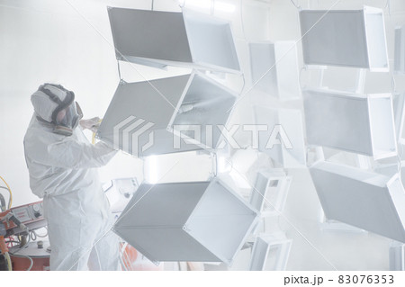 Powder coating of metal products in spray booth. Surface coating industry painting metal parts in paint booth. Coveralls worker with spray gun painting steel parts in painting chamber or paint garage Powder coating of metal products in spray booth. Surface coating industry painting metal parts in paint booth. Coveralls worker with spray gun painting steel parts in painting chamber or paint garage 83076353
