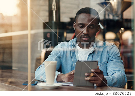 Purposeful black male entrepreneur uses tablet pc while sitting in cafe with coffee near window. Purposeful black male entrepreneur uses tablet pc while sitting in cafe with coffee near window. 83076525