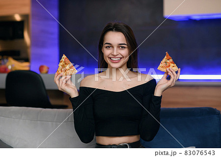 Happy beautiful girl with perfect smile having fun with pizza at home. Woman has dinner, enjoying meal. Leisure concept. 83076543