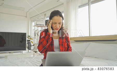 Tired latin young businesswoman have a headache. People sitting on bed with computer laptop notebook technology device in bedroom at home in early morning. Quarantine lifestyle. Unhappy life. Tired latin young businesswoman have a headache. People sitting on bed with computer laptop notebook technology device in bedroom at home in early morning. Quarantine lifestyle. Unhappy life. 83076583