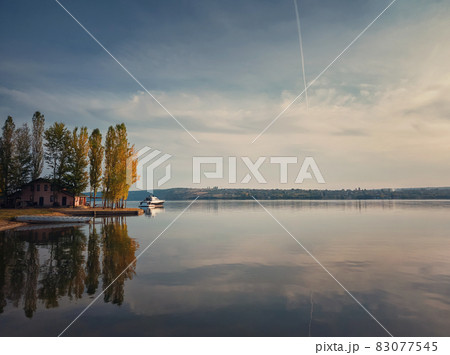 Scenic view with a house on the riverbank of Nistru river and a yacht floating. Autumn season landscape, colorful trees and beautiful sky reflected on the water surface Scenic view with a house on the riverbank of Nistru river and a yacht floating. Autumn season landscape, colorful trees and beautiful sky reflected on the water surface 83077545