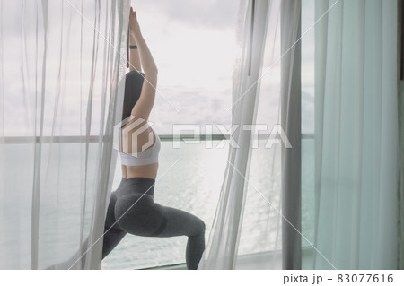 Woman does yoga warrior pose on the balcony with sea view. 83077616