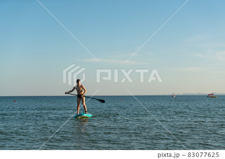 A 12 year old boy learns to stand on a SUP board in the sea near the shore. A 12 year old boy learns to stand on a SUP board in the sea near the shore. 83077625