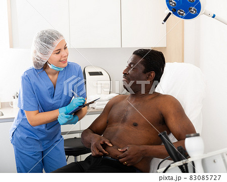 Female cosmetologist examining body of man before procedure Female cosmetologist examining body of man before procedure 83085727