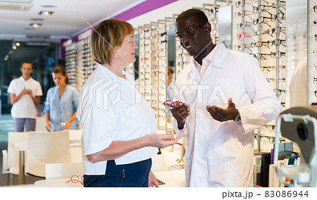 Male optician helping mature woman to choose a spectacles Male optician helping mature woman to choose a spectacles 83086944