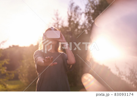 A girl holding virtual reality glasses on her head with her hands. He stretches out one hand to the camera, next to a beam of sunlight. High quality photo 83093174