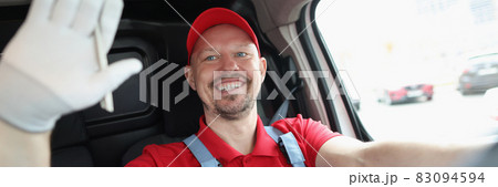 Smiling male courier driver waves his hand while driving Smiling male courier driver waves his hand while driving 83094594