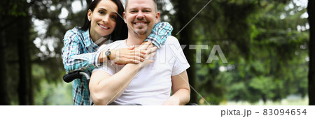 Young woman hugs disabled man in wheelchair on walk in park 83094654