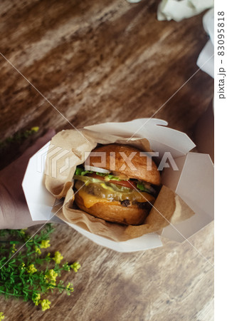 Close-up of a standard burger. Adult fast food in a restaurant or cafe. Macro photo of burger ingredients with meat, cheese and herbs. Eco burgers for the whole family 83095818