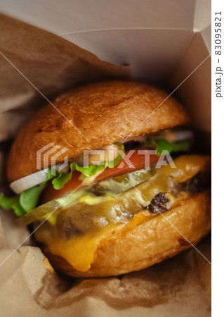Close-up of a standard burger. Adult fast food in a restaurant or cafe. Macro photo of burger ingredients with meat, cheese and herbs. Eco burgers for the whole family 83095821