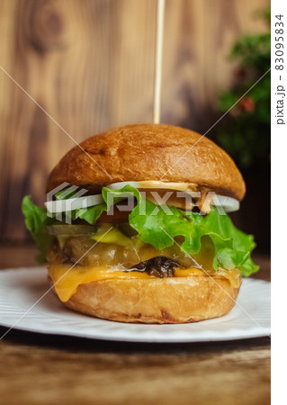 Close-up of a standard burger. Adult fast food in a restaurant or cafe. Macro photo of burger ingredients with meat, cheese and herbs. Eco burgers for the whole family 83095834