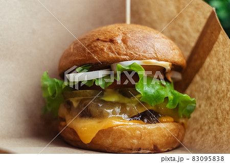 Close-up of a standard burger. Adult fast food in a restaurant or cafe. Macro photo of burger ingredients with meat, cheese and herbs. Eco burgers for the whole family 83095838