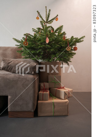 Small christmas tree with natural decorations and presents indoor near couch with warm light 83097323