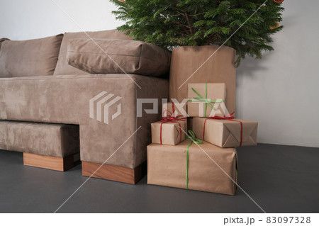presents in paper wrap with ribbons under christmas tree indoor near couch with warm light 83097328