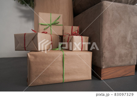 presents in paper wrap with ribbons under christmas tree indoor near couch with warm light 83097329