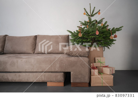 Small christmas tree with natural decorations and presents indoor near couch with window light 83097331