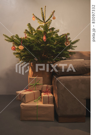 Small christmas tree with natural decorations and presents indoor near couch with warm light 83097332