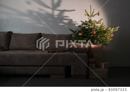 Small christmas tree with natural decorations and presents indoor near couch with warm light 83097333