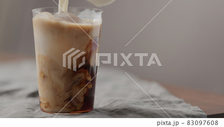 milk pour cold in brew coffee in tumbler glass on walnut table milk pour cold in brew coffee in tumbler glass on walnut table 83097608