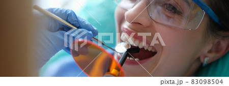 Doctor dentist treating teeth using LED curing light machine in clinic closeup 83098504