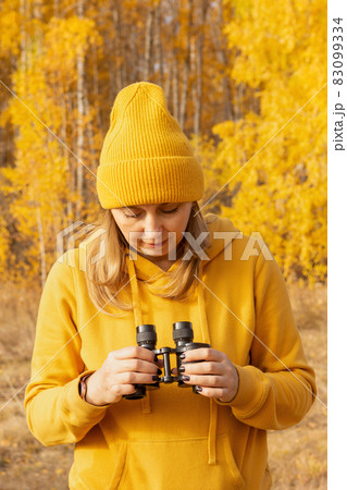 A beautiful positive woman in yellow clothes with binoculars on a picnic in the woods on an autumn day. The concept of the road, freedom, rest, travel 83099334