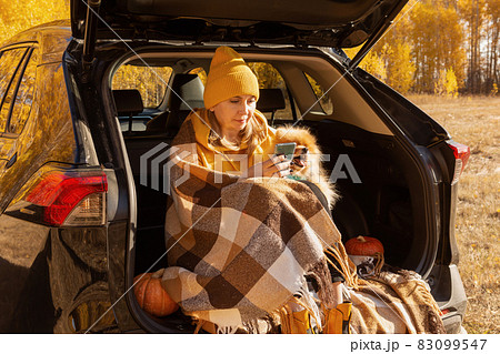 A beautiful positive woman in yellow clothes at a picnic sitting in the trunk of a car with her dog pomeranian takes a selfie on an autumn day. A beautiful positive woman in yellow clothes at a picnic sitting in the trunk of a car with her dog pomeranian takes a selfie on an autumn day. 83099547