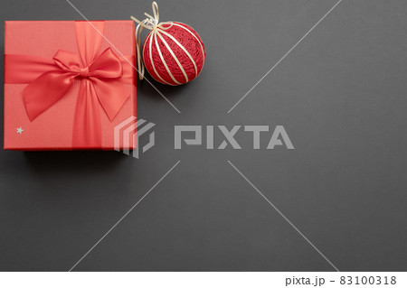 Gift red box with a bow and a handmade Christmas ball in the upper corner on a dark gray background. Christmas mockup. Top view Gift red box with a bow and a handmade Christmas ball in the upper corner on a dark gray background. Christmas mockup. Top view 83100318
