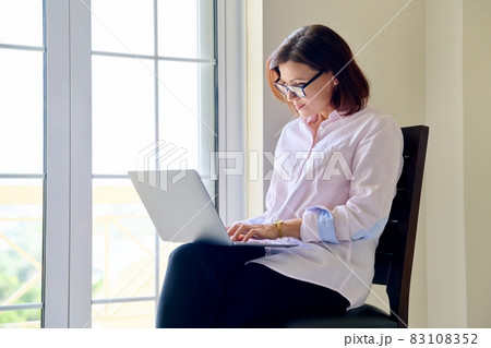 Mature businesswoman in glasses with laptop in her hands near window 83108352