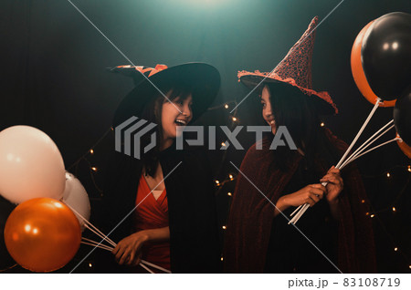 Portrait of two beautiful young woman in witch halloween costumes holding balloons in party over dark magic background - Halloween party concept. Portrait of two beautiful young woman in witch halloween costumes holding balloons in party over dark magic background - Halloween party concept. 83108719