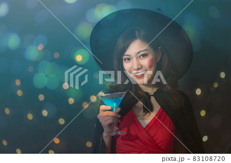 Portrait of beautiful young asian woman in witch halloween costumes drinking cocktail in halloween party over dark magic background - holiday party concept. Portrait of beautiful young asian woman in witch halloween costumes drinking cocktail in halloween party over dark magic background - holiday party concept. 83108720