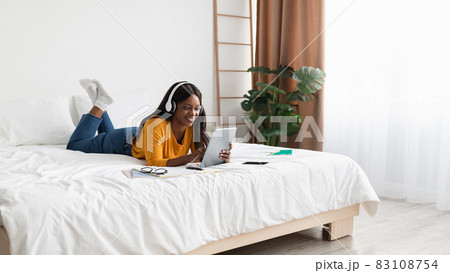 Black Woman Using Tablet Wearing Earphones Learning In Bedroom, Panorama Black Woman Using Tablet Wearing Earphones Learning In Bedroom, Panorama 83108754