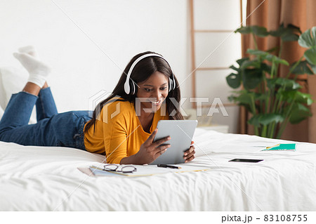 African American Female Student Using Tablet Wearing Headphones At Home African American Female Student Using Tablet Wearing Headphones At Home 83108755