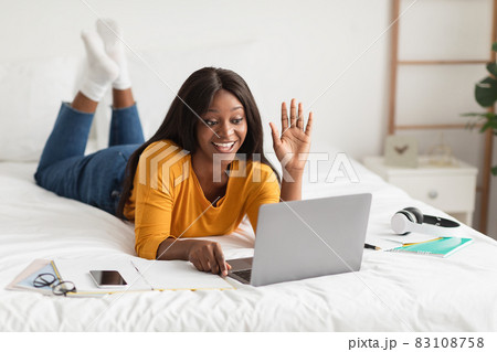African Woman Video Calling Waving Hello To Laptop In Bedroom African Woman Video Calling Waving Hello To Laptop In Bedroom 83108758