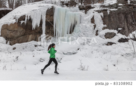 Winter run sport woman running on snow trail training cardio outdoors on cold weather. Asian runner girl working out outside wearing leggings and active coat 83108902