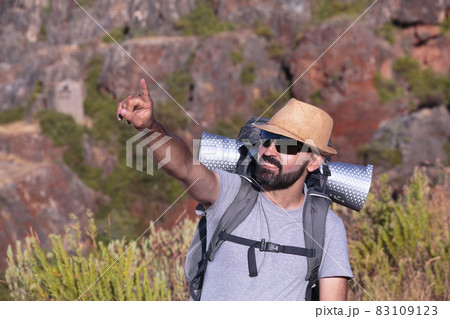 Hispanic male trekker with sunglasses smiling and pointing out of the frame 83109123