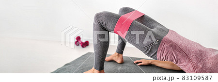 Fitness resistance band glute bridge with hip abduction exercise woman workout at home. Fit girl training with circle hoop booty bands for glute strengthening banner panorama 83109587