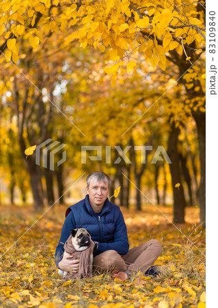 A man with his beloved pug dog on a walk in the autumn in the park 83109840